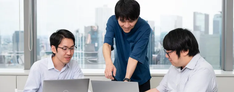 オフィスでノートパソコンを囲んで話し合う社員たち